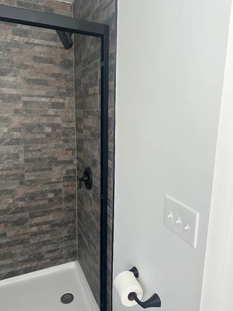 Black-framed glass shower enclosure with gray stacked slate tile walls and white drywall