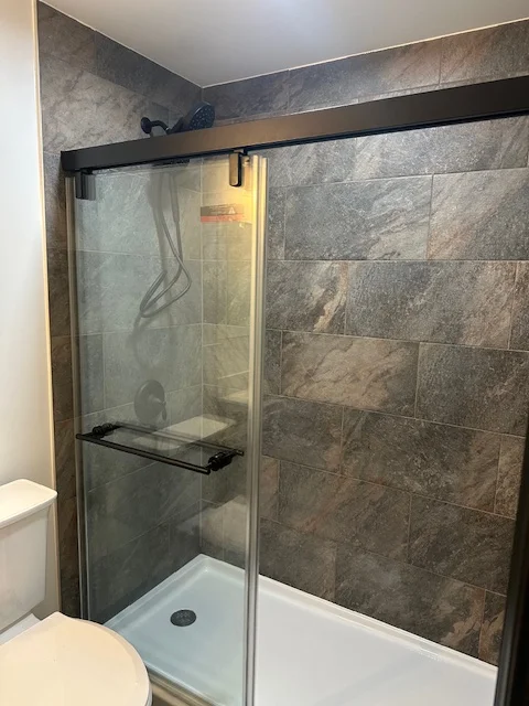 Gray tile shower with frameless glass enclosure and black metal framing