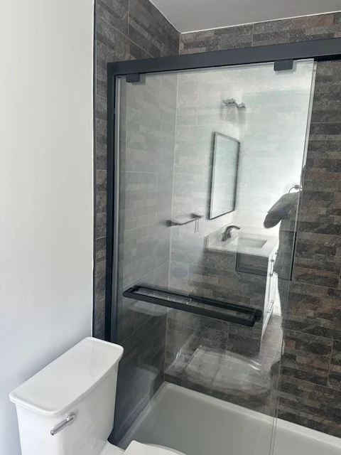Dark gray tile bathroom with frameless glass shower enclosure and black hardware