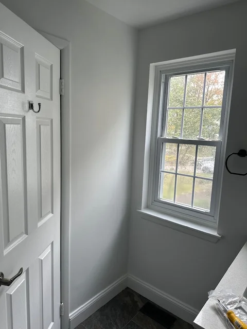 Interior bedroom with white painted door and trim, gray walls, and double-hung window