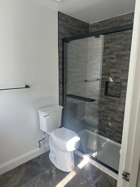 Bathroom with white painted walls, dark gray tile shower surround, and modern white toilet