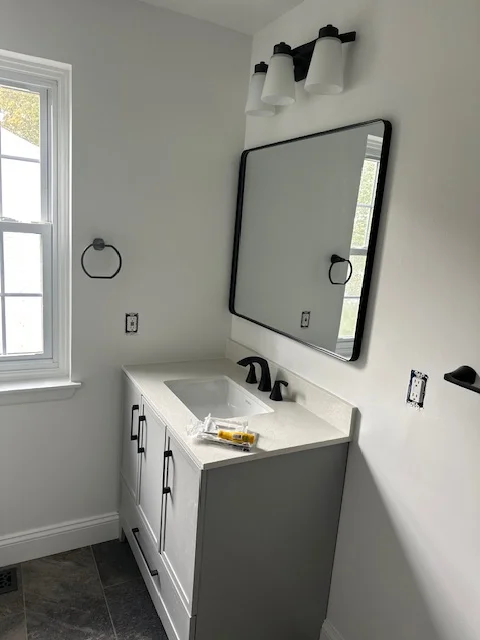 Newly painted bathroom with gray walls, black-framed mirror, white vanity, and modern black fixtures