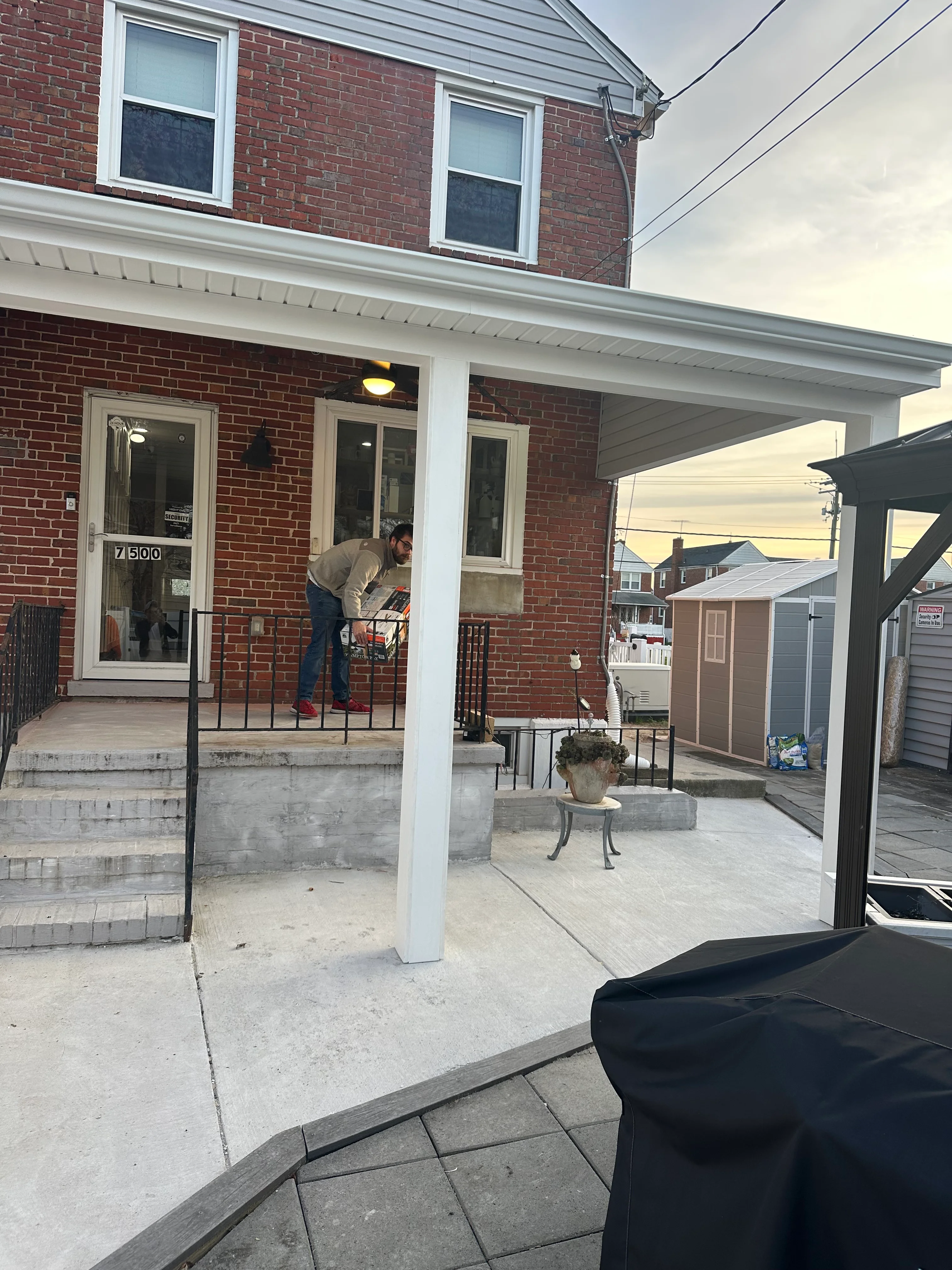 Red brick home with white-trimmed windows and freshly painted white porch columns and concrete patio