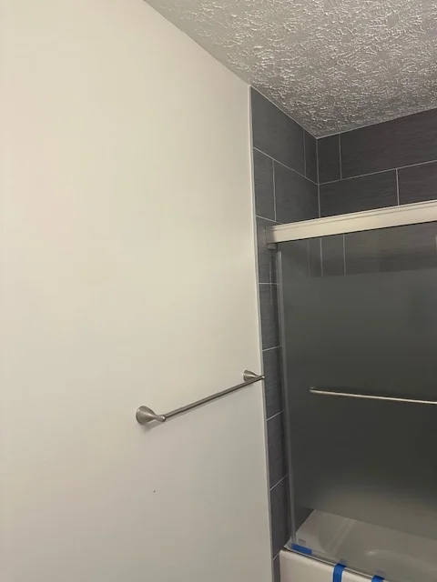 Bathroom with white painted walls, dark subway tile shower, textured ceiling, and chrome towel bar