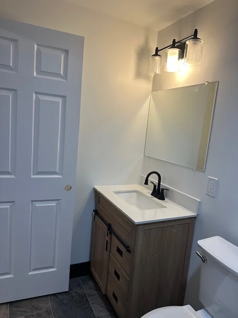 Bathroom with white painted walls, white six-panel door, wood vanity, and black vanity lighting fixture