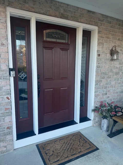 Burgundy painted entry door with white trim and sidelights on brick home exterior