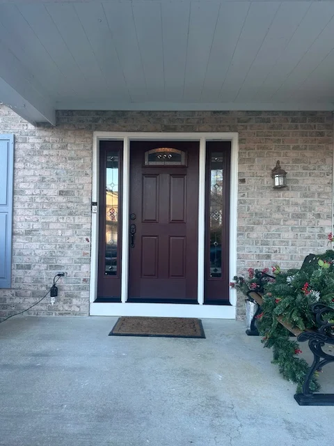 Deep burgundy six-panel entry door with white trim and sidelights on brick facade